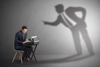 Bărbat pe scaun lucrând sub semnul fricii, fiind amenințat de superiori.