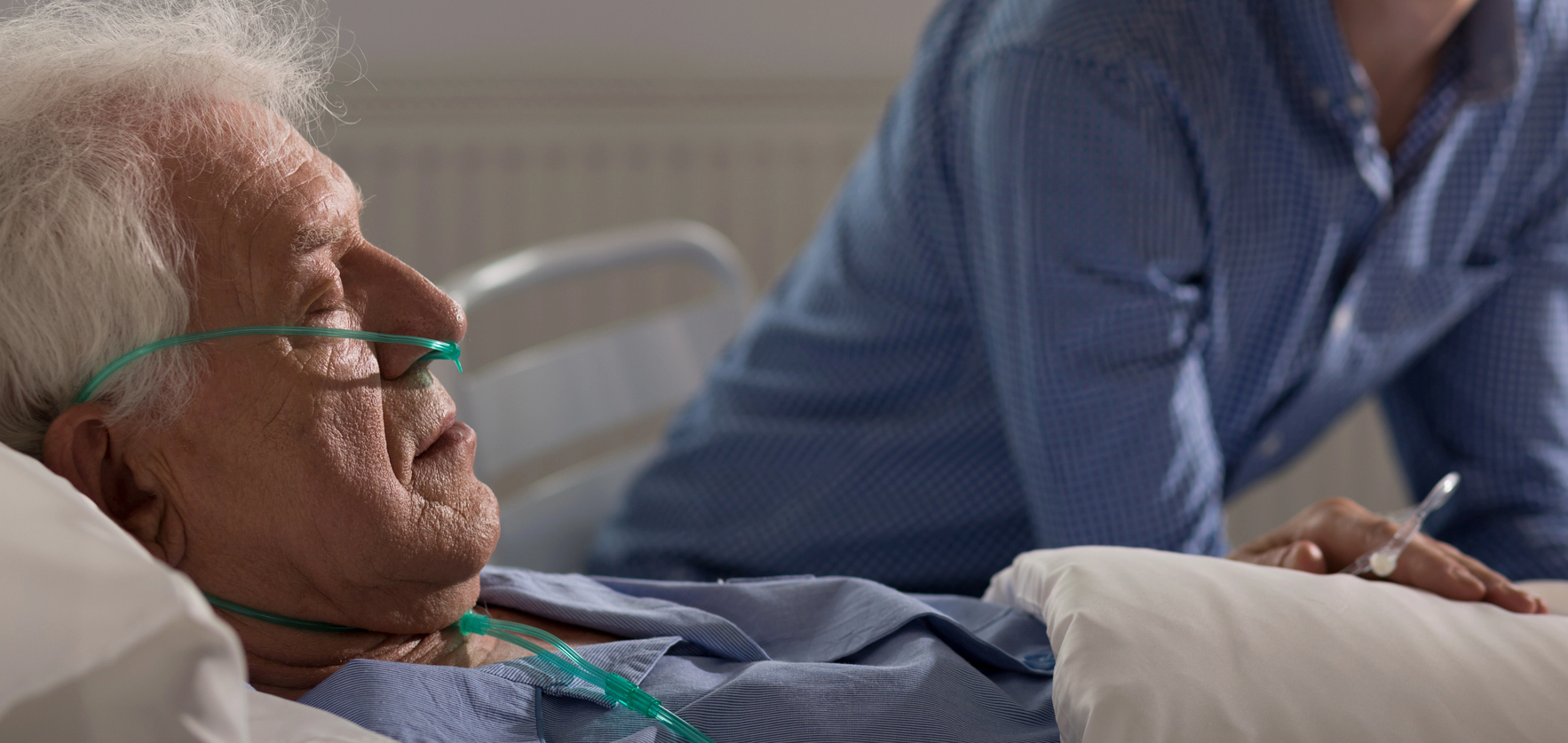 Pacient vârstnic pe pat de spital asistat de aparținător, imagine din sistemul sanitar din România
